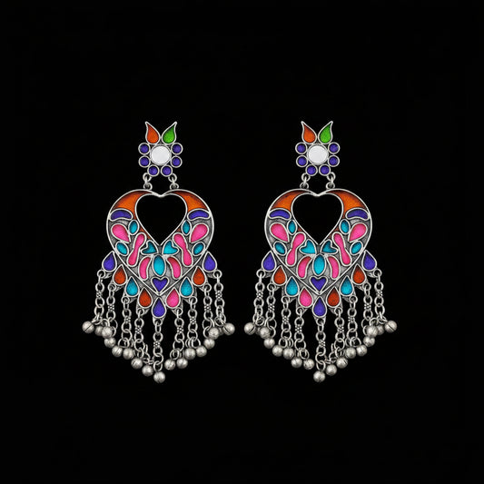 A pair of silver-toned Indian chandbali earrings decorated with vibrant pink, blue, orange, and green enamel, featuring dangling silver bells on a dark reflective surface.