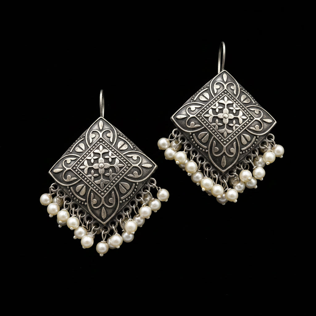 A pair of silver-toned geometric dangle earrings with intricate filigree cutouts and cascading pearl-like beads, displayed on a clean white background with the brand logo 'SAHELI MY BEST FRIEND' at the top.