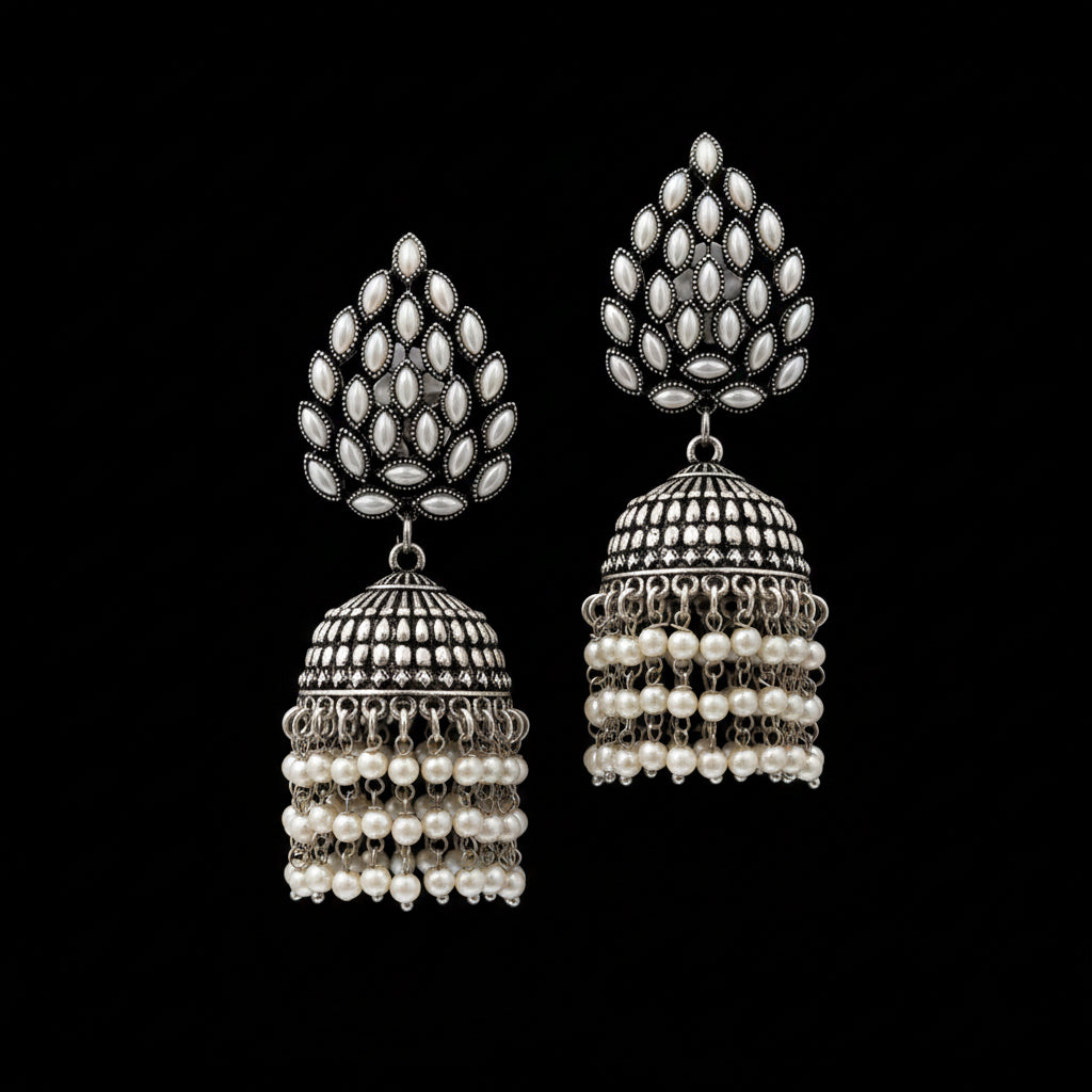 A pair of traditional Indian silver-toned jhumka earrings with white pearl bead fringe, displayed on a black stand against a white background. The brand logo 'SAHELI MY BEST FRIEND' is visible in the top left corner.