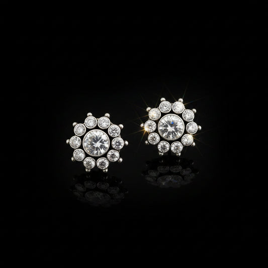 A pair of silver-toned stud earrings with clear round-cut gemstones arranged in a floral or snowflake-like cluster, displayed on a dark reflective surface with the SAHELI MY BEST FRIEND logo above.