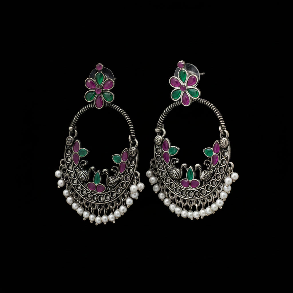 Pair of silver earrings with floral designs on a dark background