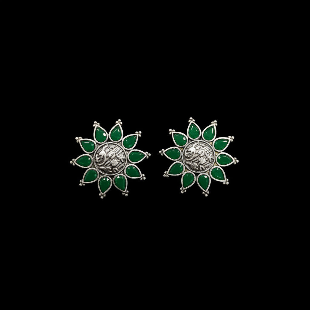 A pair of silver-toned crescent moon earrings with green enamel petals, displayed on a textured blue surface with gold Al-Rawnaq branding. A small white price tag is attached to one earring.