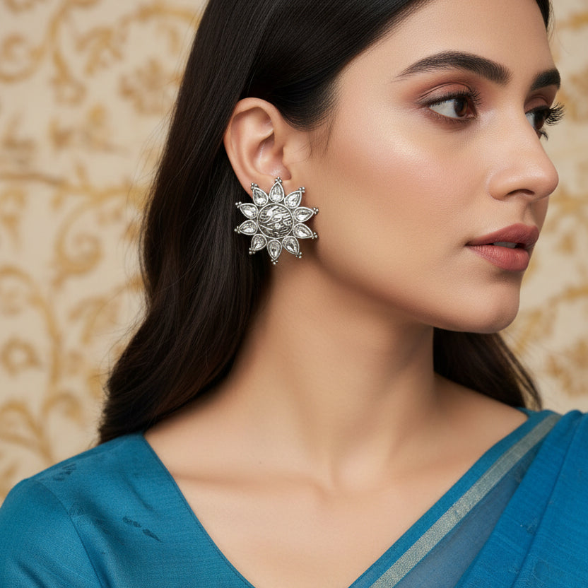 Silver earrings with clear stones on a blue background with 'Al-Rawnaq' branding.