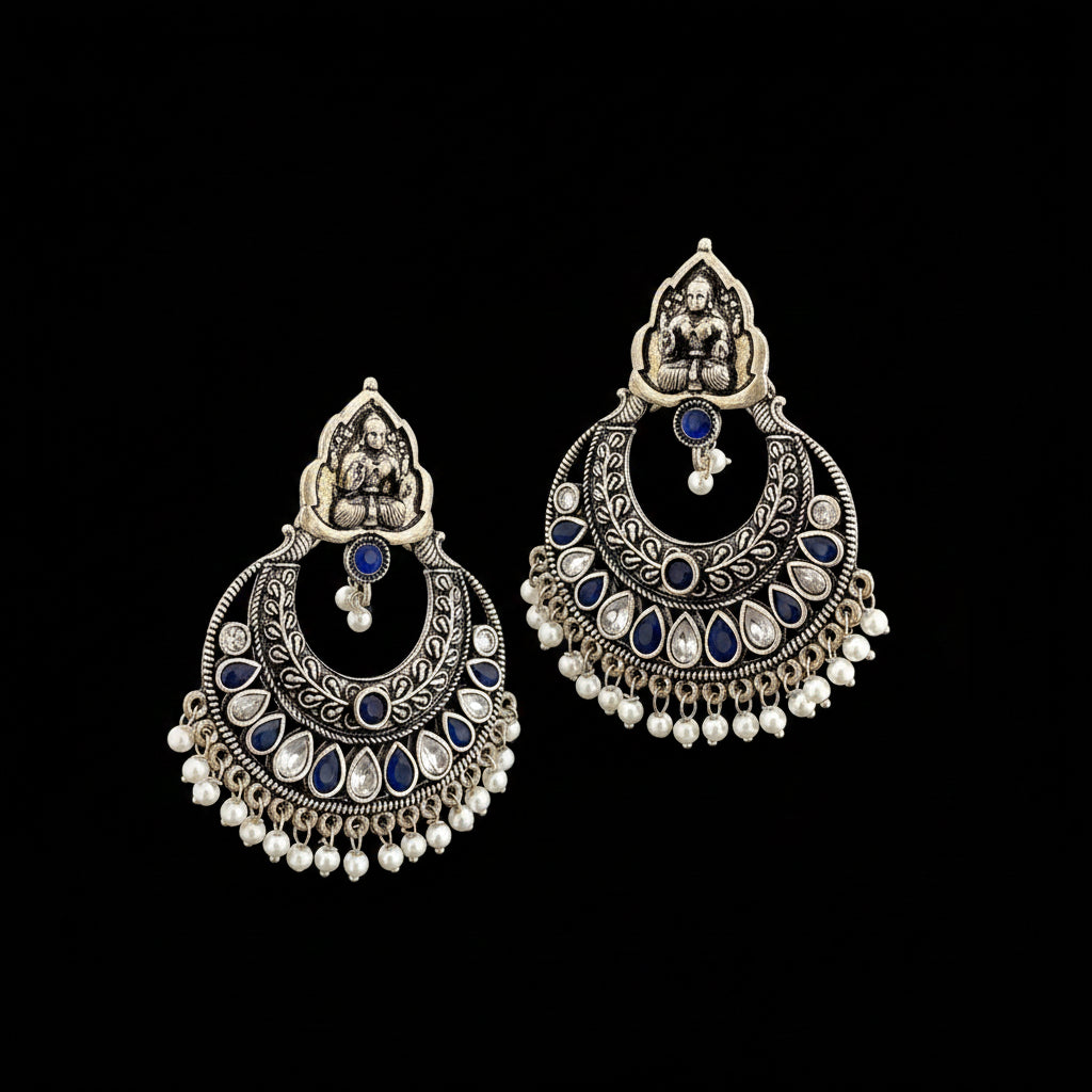 A pair of traditional Indian silver-toned chandbali earrings with blue stone accents and white bead fringe, displayed on a dark reflective surface with the brand logo 'SAHELL MY BEST FRIEND' above them.