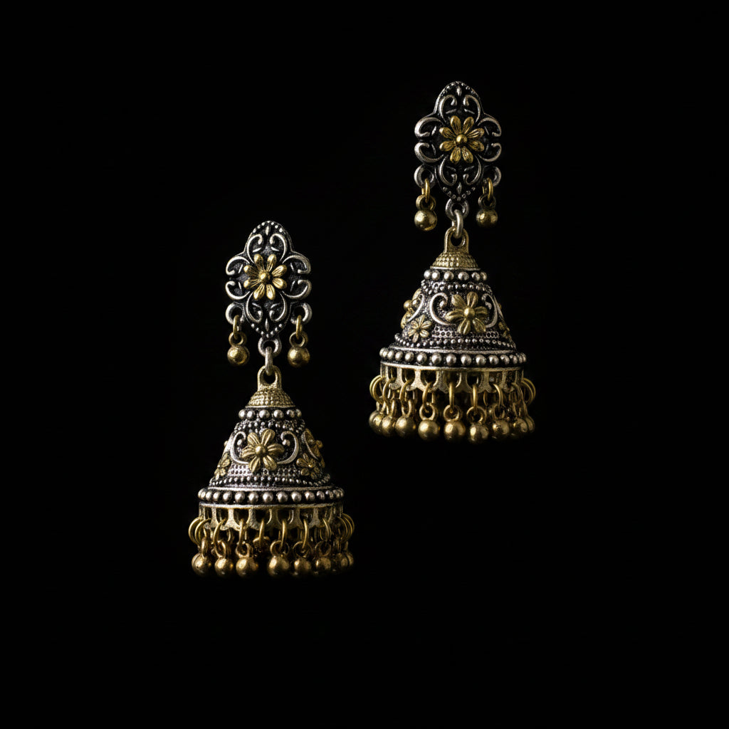 A pair of traditional Indian jhumka earrings displayed on a gray velvet jewelry stand. The earrings feature intricate filigree detailing in silver and gold metals, with dangling bell-shaped charms and small hanging bells at the bottom.