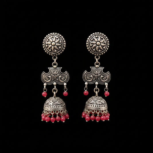 A pair of traditional Indian silver-toned jhumka earrings with red bead accents, displayed on a gray Y-shaped stand against a neutral gray background. The brand logo 'SAHELL MY BEST FRIEND' is visible at the top center.