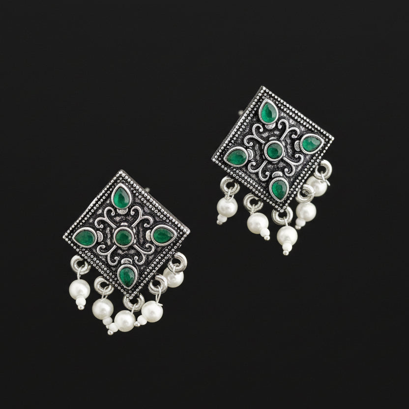 Pair of silver earrings with green gemstones and white beads on a gray background