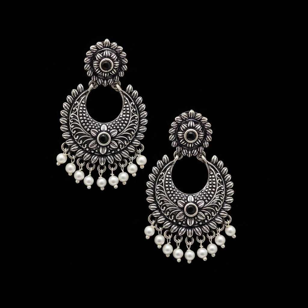 Ornate silver earrings with pearl drops on a gray background, featuring the brand 'Saheli'.