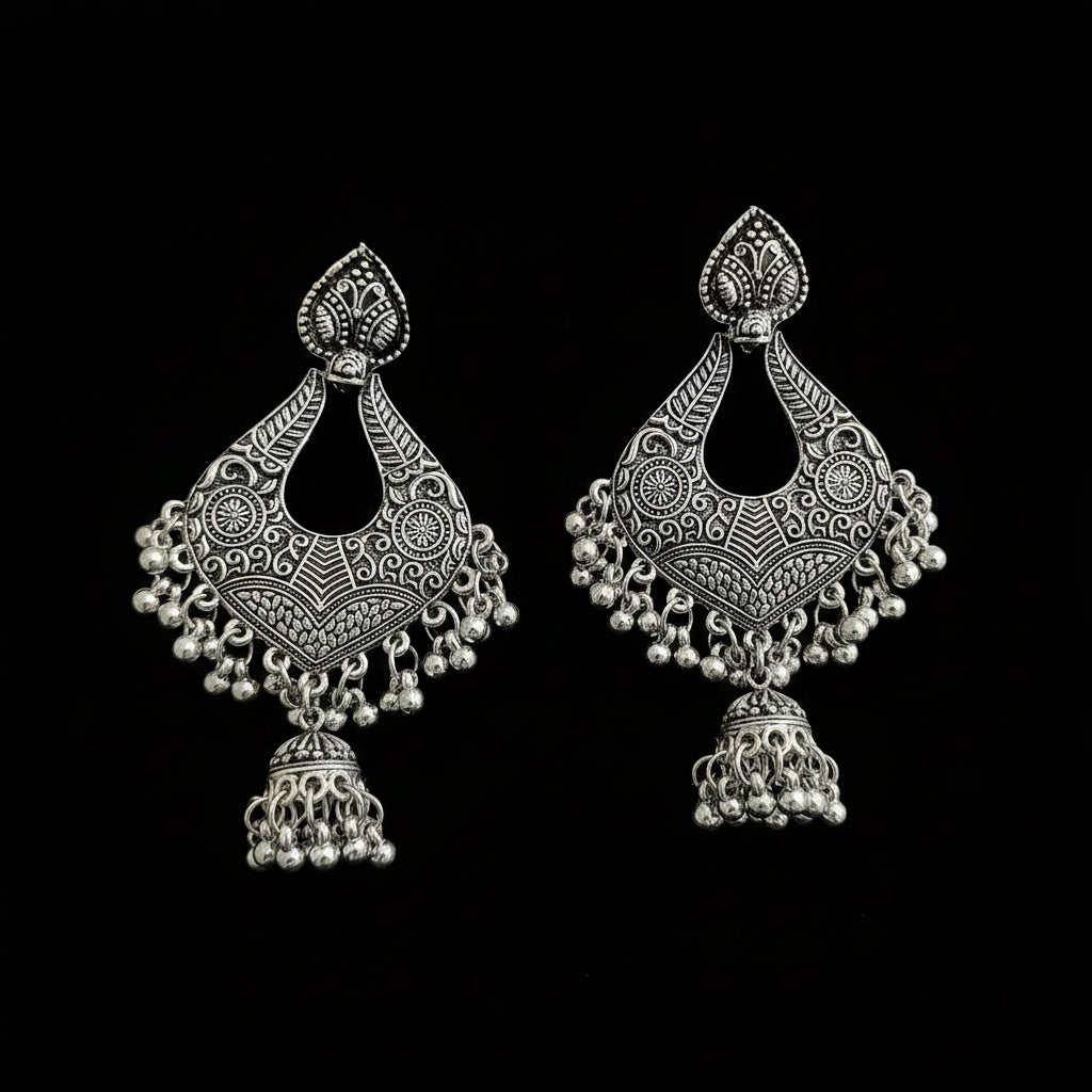 A pair of ornate silver-toned Indian jhumka earrings with intricate filigree work and dangling bead chains, displayed on a dark reflective surface.