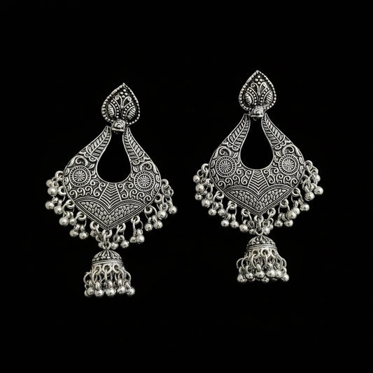 A pair of ornate silver-toned Indian jhumka earrings with intricate filigree work and dangling bead chains, displayed on a dark reflective surface.