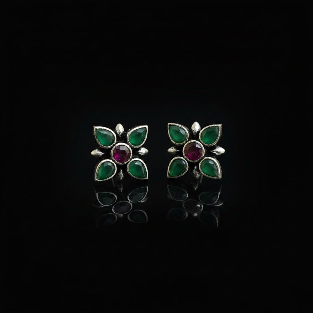 Pair of flower-shaped earrings with green and purple accents on a reflective surface.