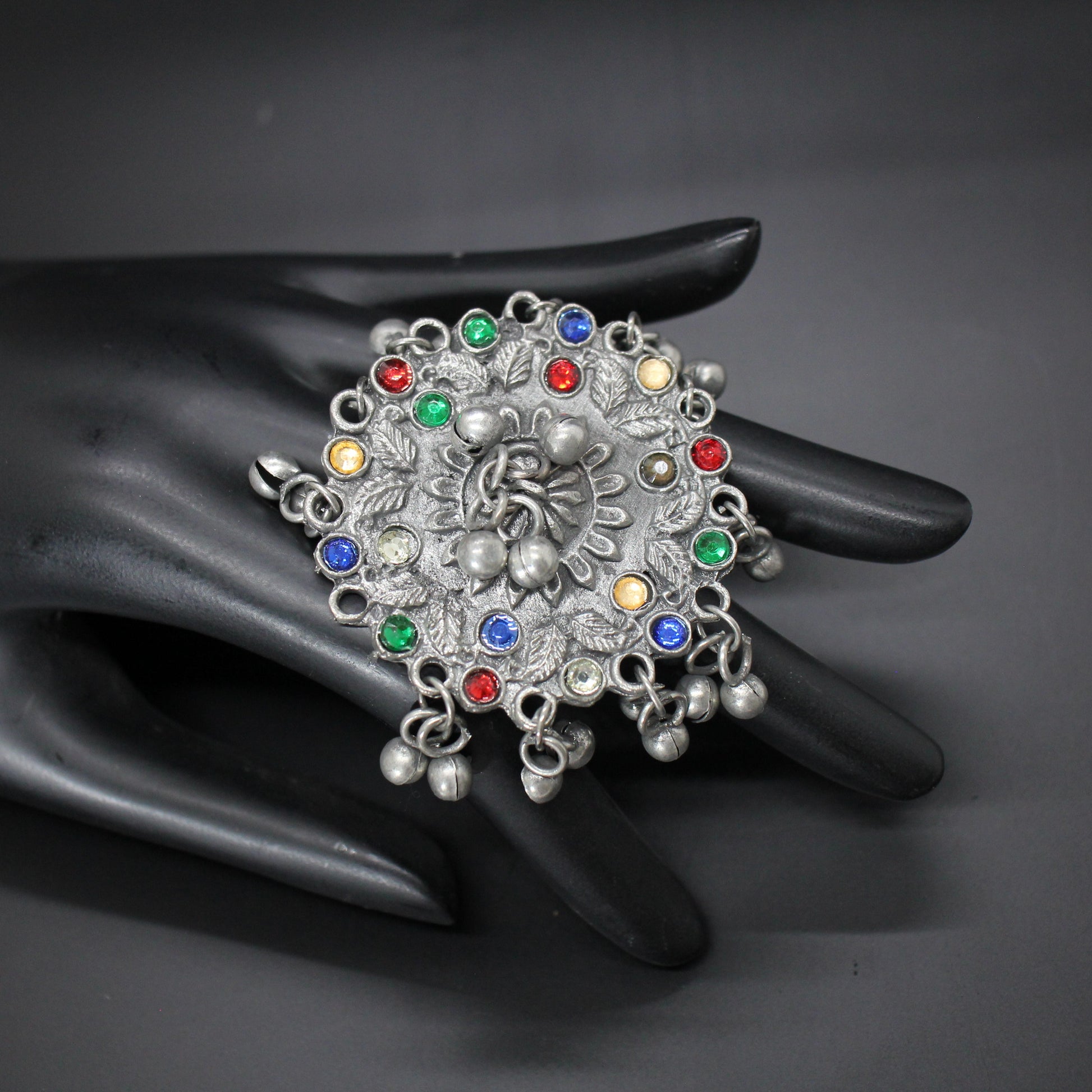 Decorative ring with multicolored gemstones on a black mannequin hand against a dark background
