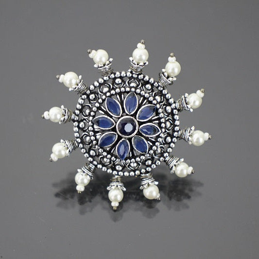 Decorative brooch with blue center and pearl-like accents on a gray background
