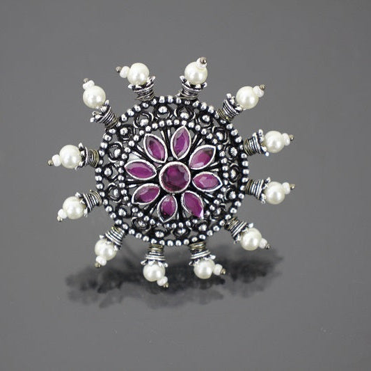 Jewelry item with purple center and pearl-like accents on a gray background