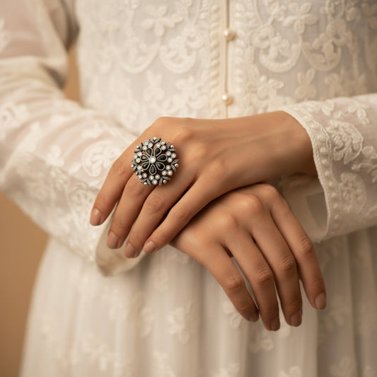 Silver ring with floral design on a black mannequin hand, branded 'SAHELI'.