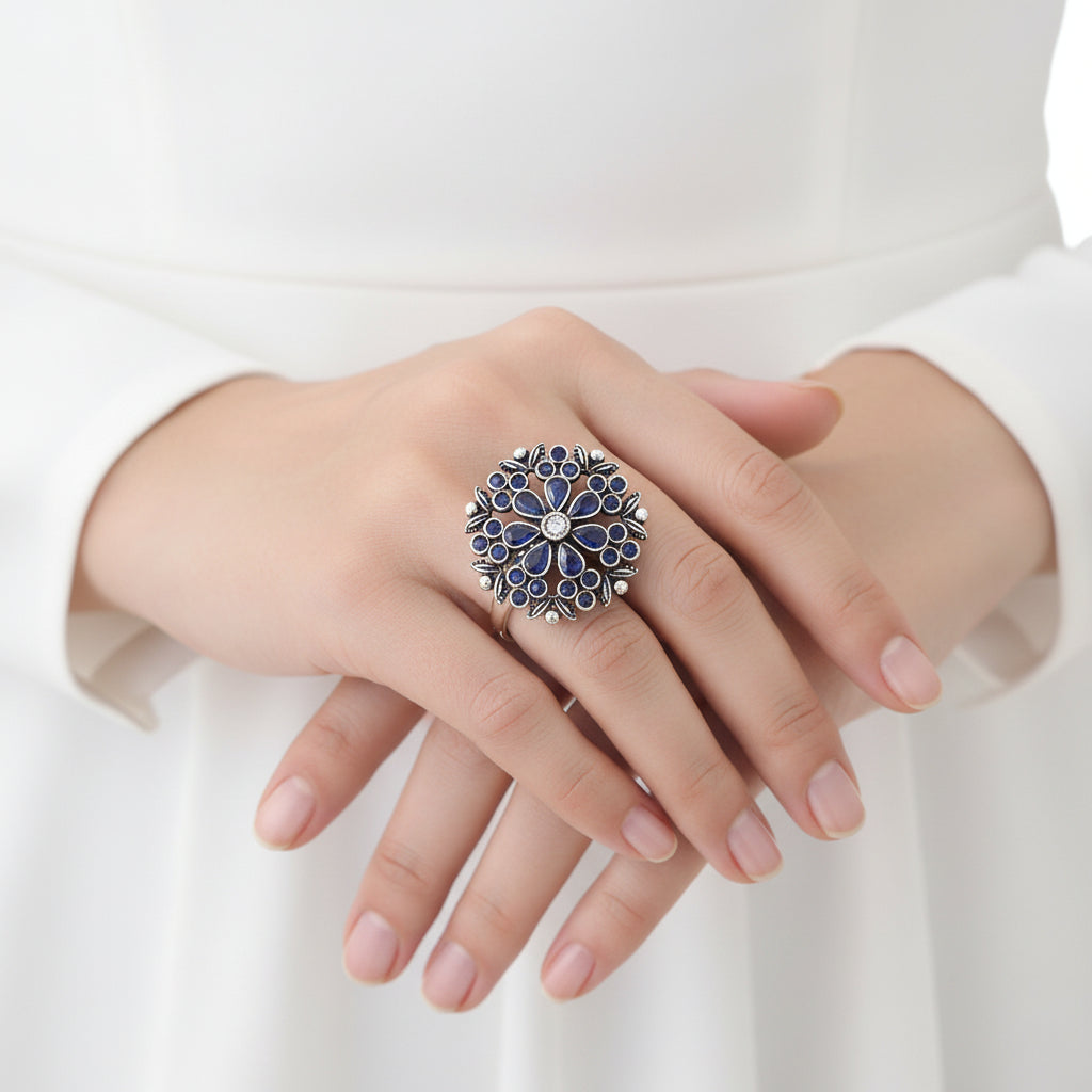 Silver ring with blue stones on a black mannequin hand, branded 'Saheli'.