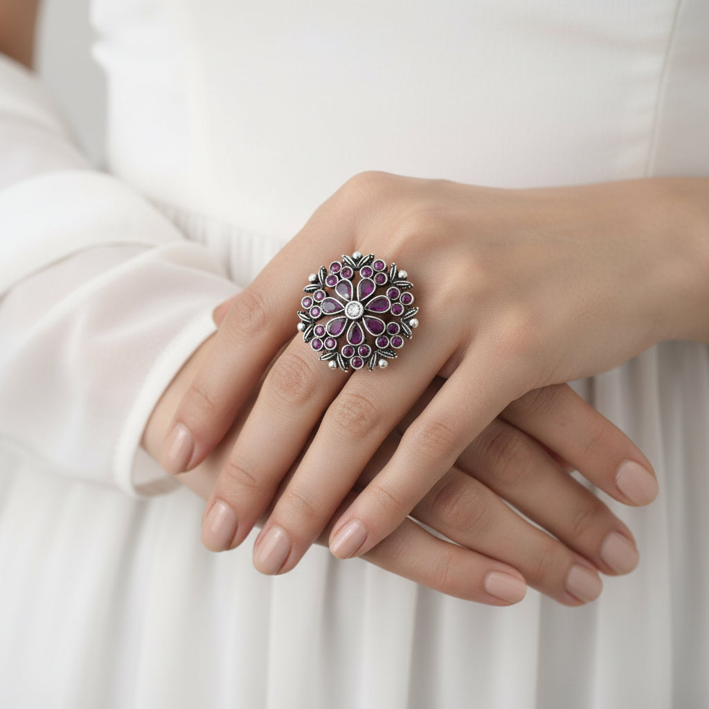 Decorative ring with pink gemstones on a black mannequin hand, branded 'Saheli'.