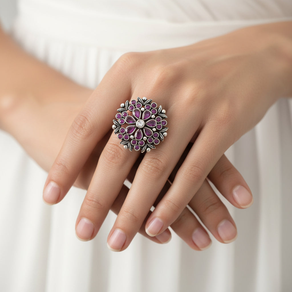 Decorative ring with pink gemstones on a black mannequin hand, branded 'Saheli'.