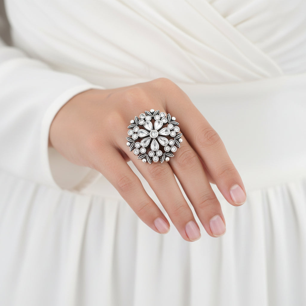 Silver ring with floral design on a black mannequin hand, branded 'Saheli'.