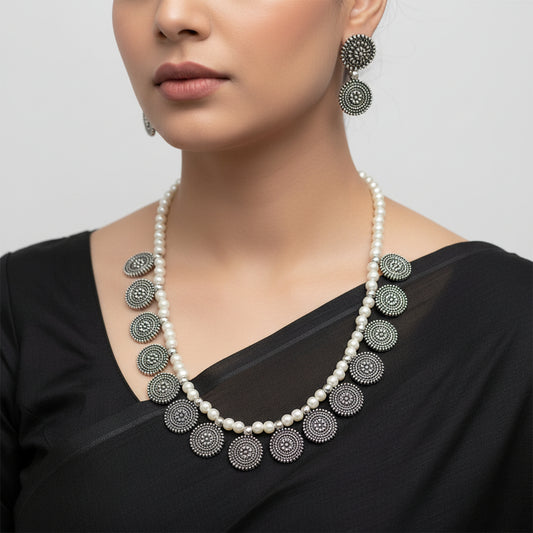 Pearl necklace with black circular pendants and matching earrings on a white background, branded 'Saheli'.