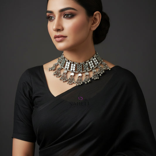 Silver necklace with dangling beads on a black background, featuring the brand 'Saheli'.