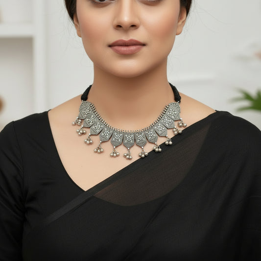 Silver necklace with intricate designs and dangling beads on a reflective surface
