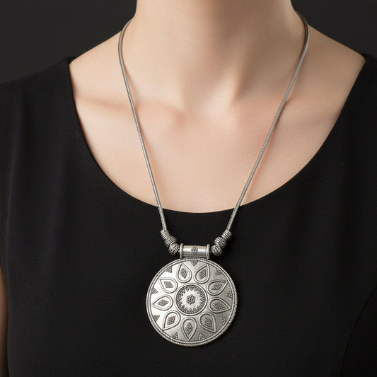 Silver necklace with a decorative pendant on a dark background, featuring the brand 'Saheli'.