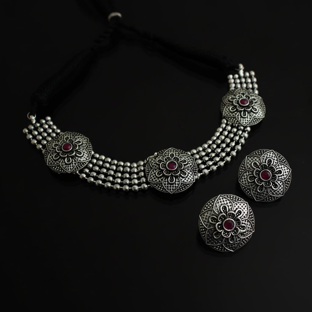 Silver necklace with floral designs and red stones on a dark background