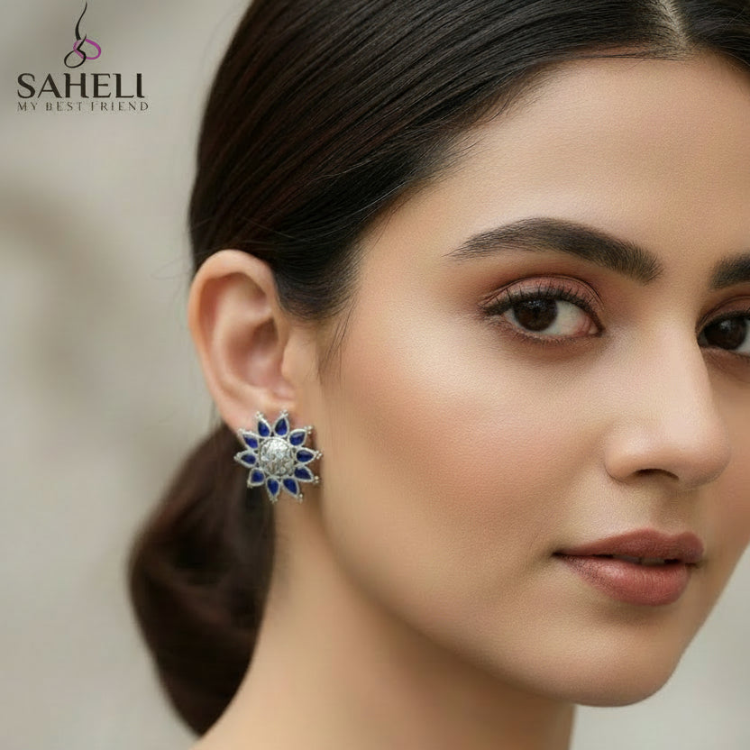 Silver and blue floral earrings on a gray background with 'Saheli' branding.
