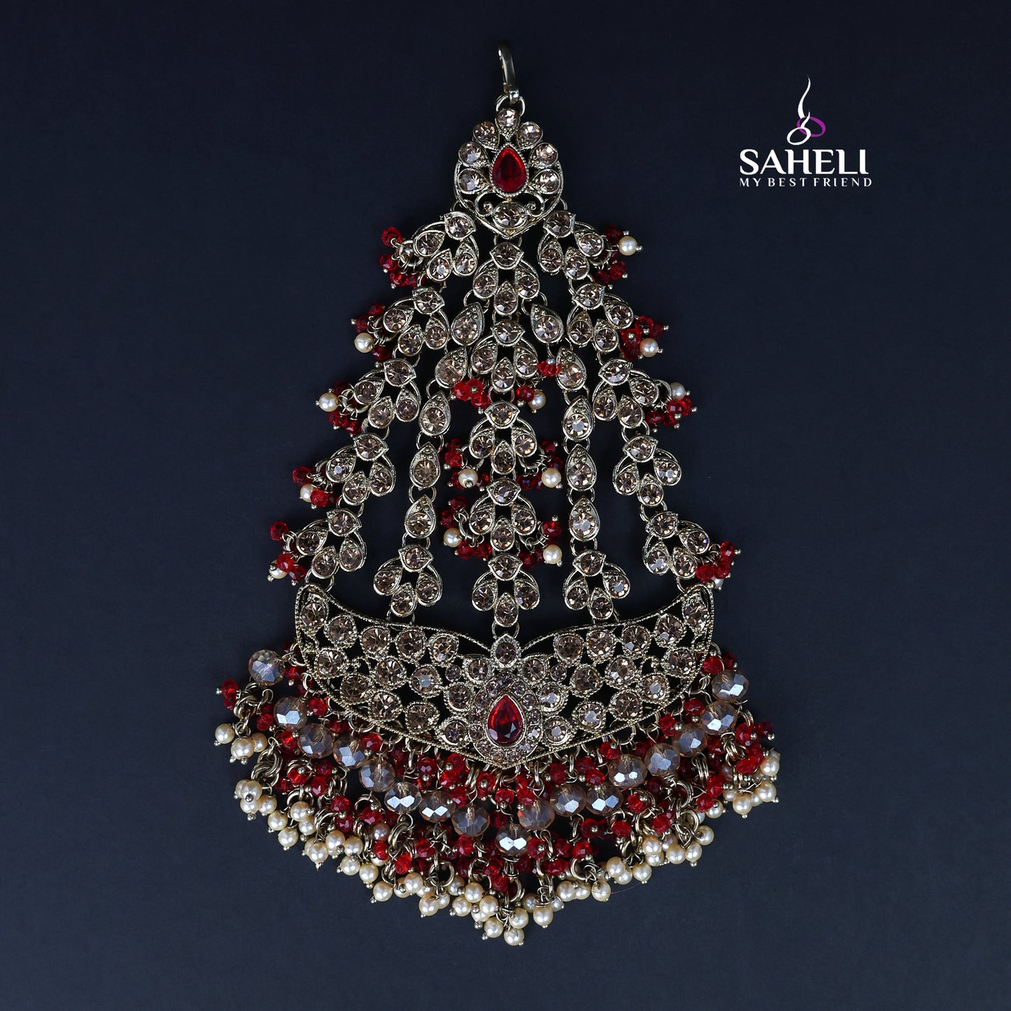 Ornate silver and red jewelry piece with 'SAHELI' branding on a dark background