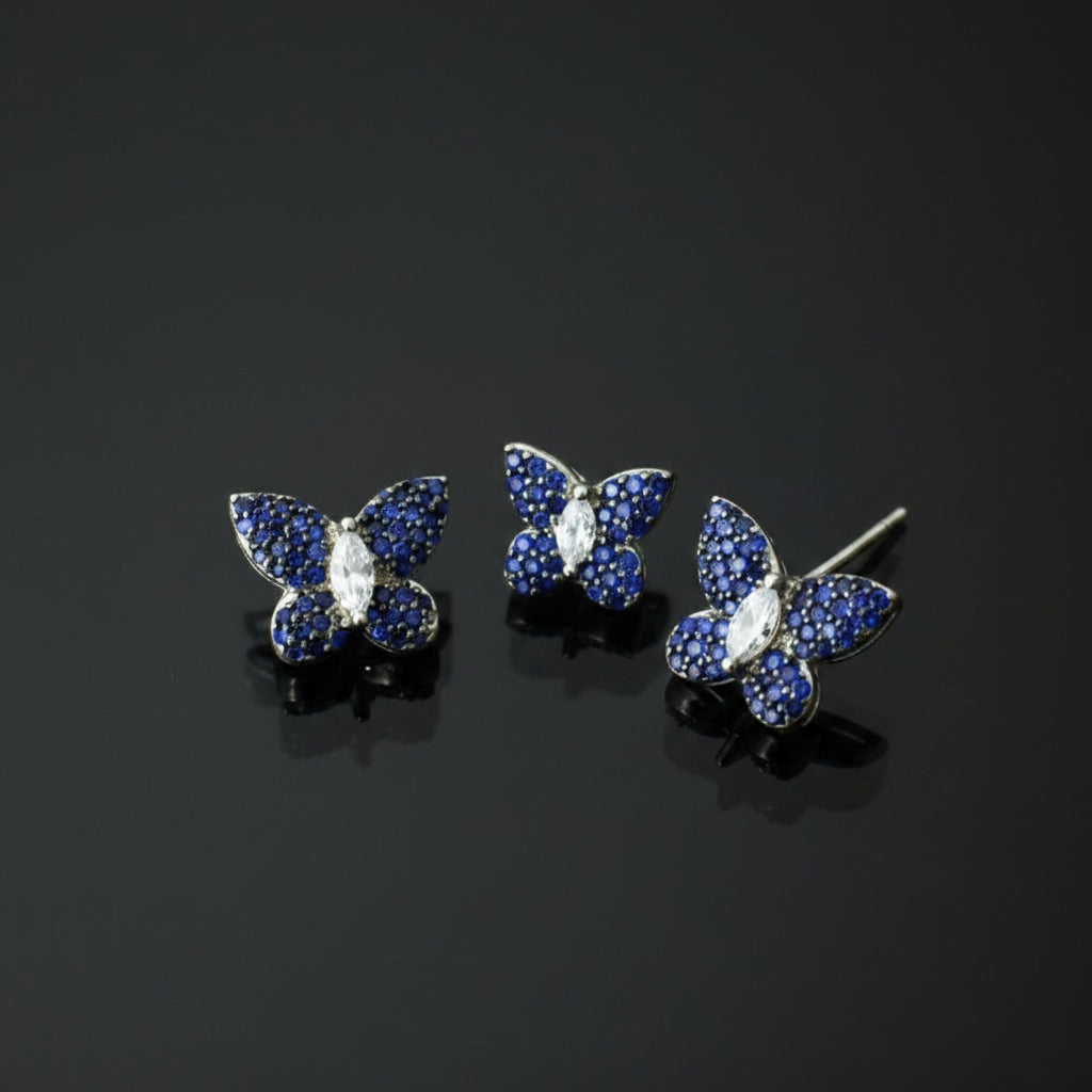 Butterfly-shaped jewelry set with blue gemstones on a gray background, featuring the brand 'Saheli'.