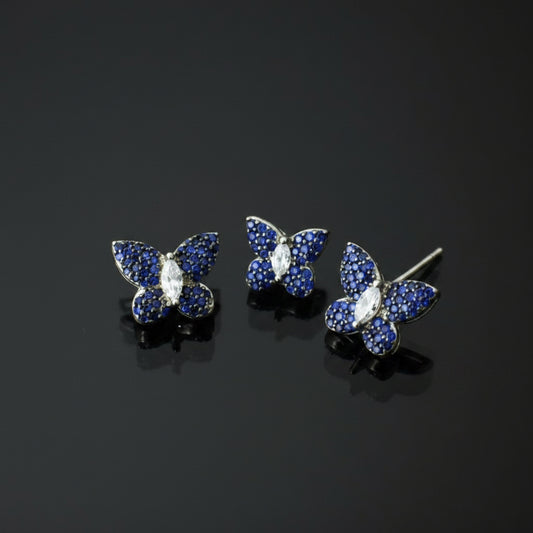 Butterfly-shaped jewelry set with blue gemstones on a gray background, featuring the brand 'Saheli'.