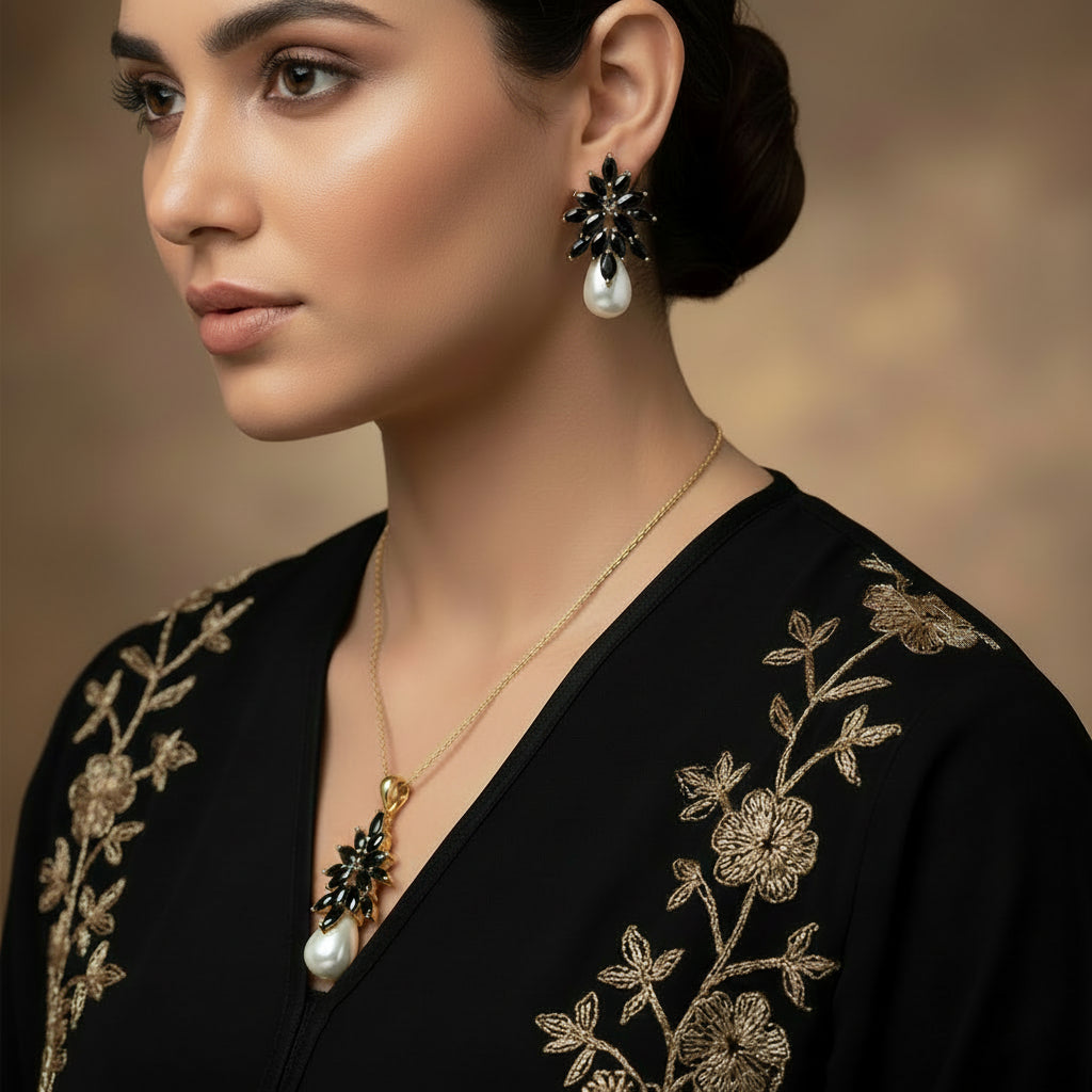 Gold and black earrings with pearl drops on a dark background, branded 'Saheli'.
