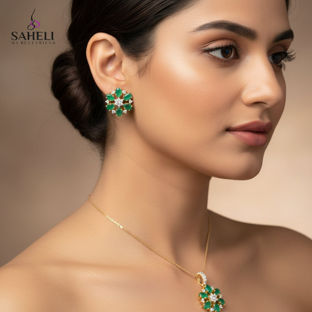 Pair of emerald and diamond earrings on a gray background with 'Saheli' branding.