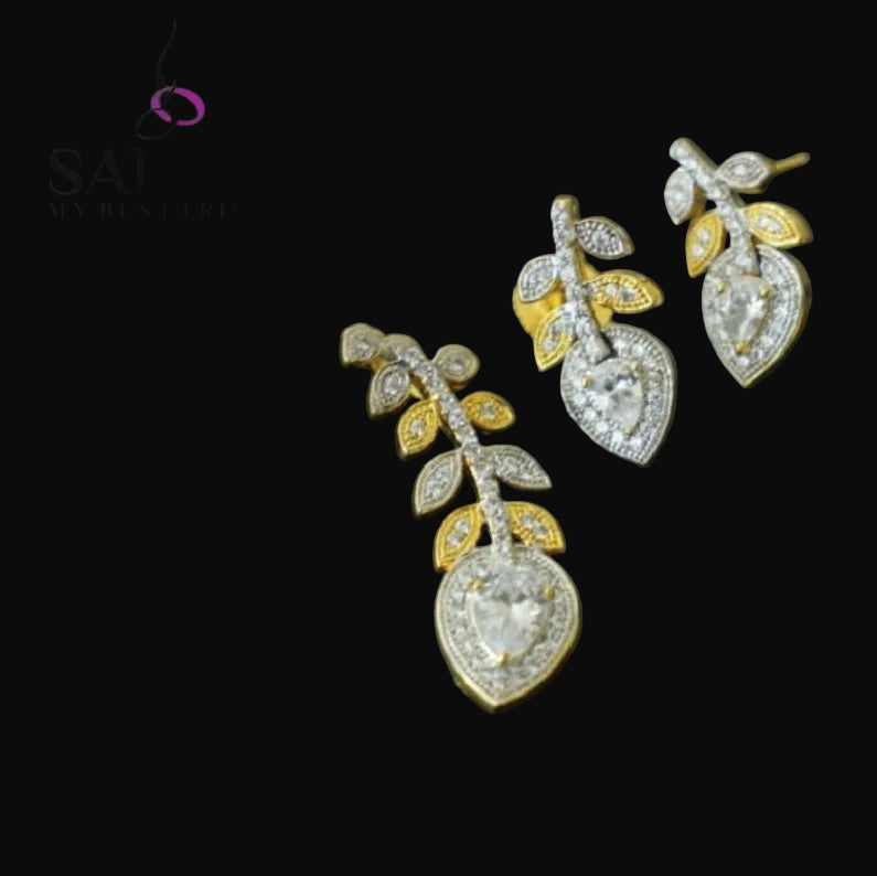 Pair of diamond earrings with gold and silver accents on a dark background, featuring the brand 'Saheli'.