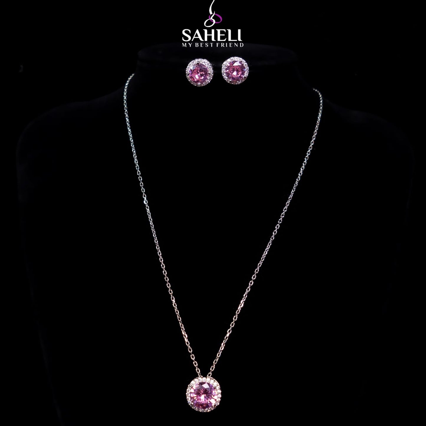 Jewelry set with pink pendant necklace and earrings on a black background, featuring the brand 'Saheli'.