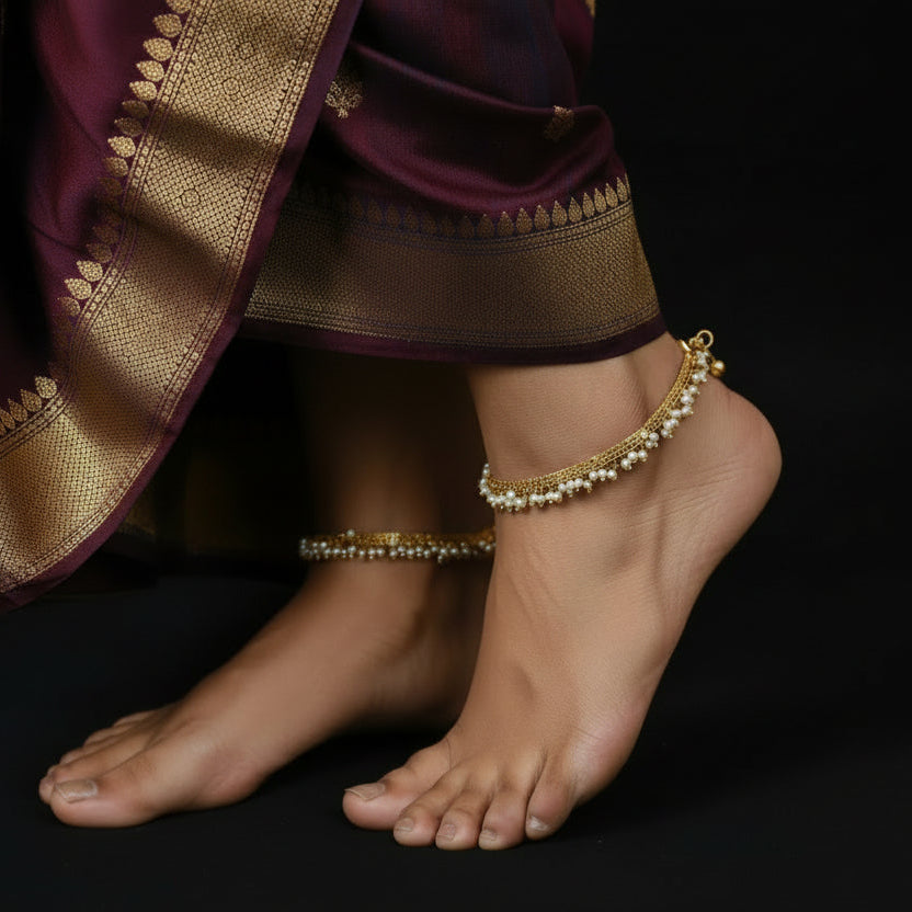 Gold anklet with pearls on a dark background, featuring the brand 'Saheli'.