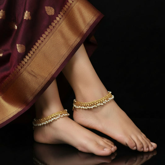 Gold necklace with pearl-like beads on a dark background, featuring the brand 'Saheli'.