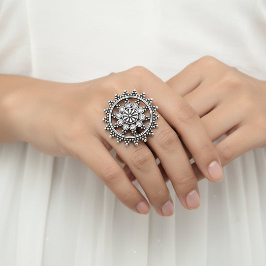 Silver ring with floral design on a gray background, featuring the brand 'Saheli'.