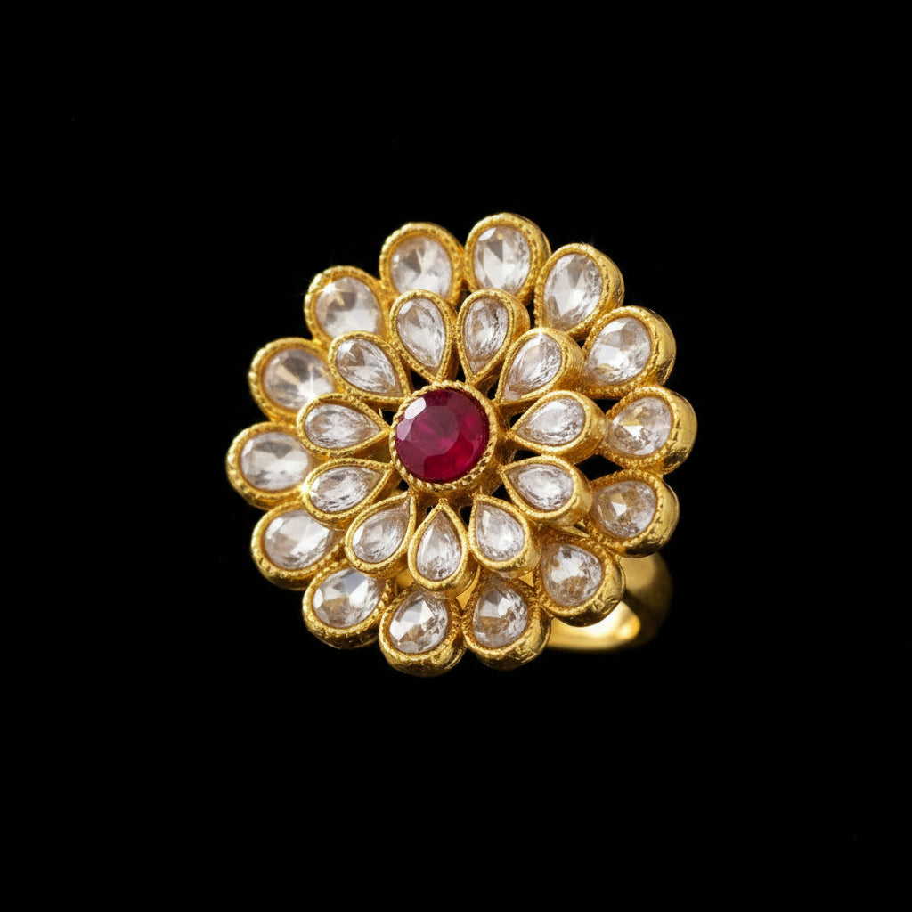 A gold-toned floral kanzulak stone embellishment featuring a central red oval stone surrounded by clear teardrop-shaped stones, displayed on a neutral gray background with a 'SAHELI MY BEST FRIEND' logo in the top-left corner.