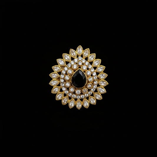 A gold-toned floral brooch featuring a central black teardrop-shaped stone surrounded by clear marquise and round crystals, displayed on a dark reflective surface with the SAHELL MY BEST FRIEND logo in the top left corner.