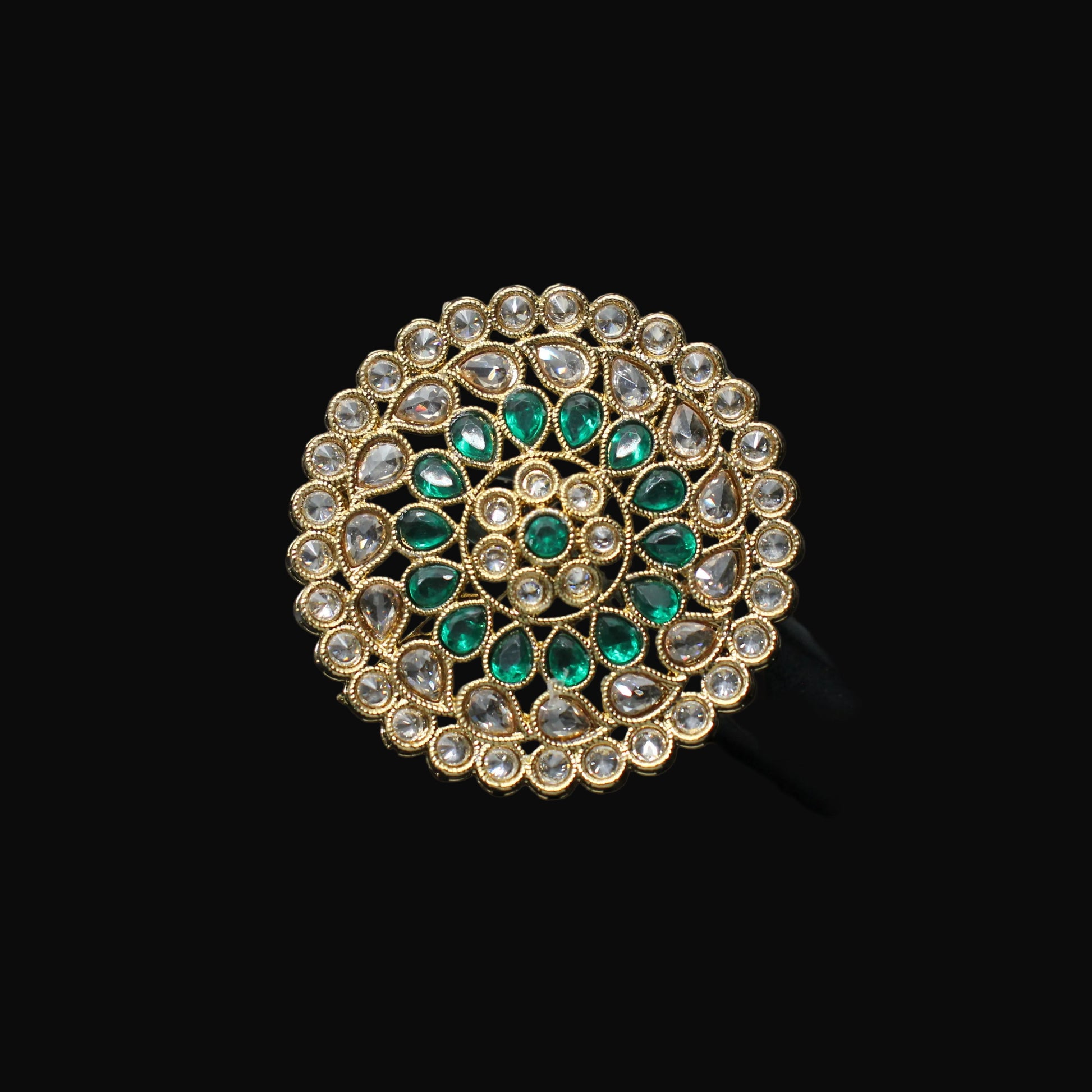 Decorative brooch with green gemstones and gold accents on a black mannequin hand.
