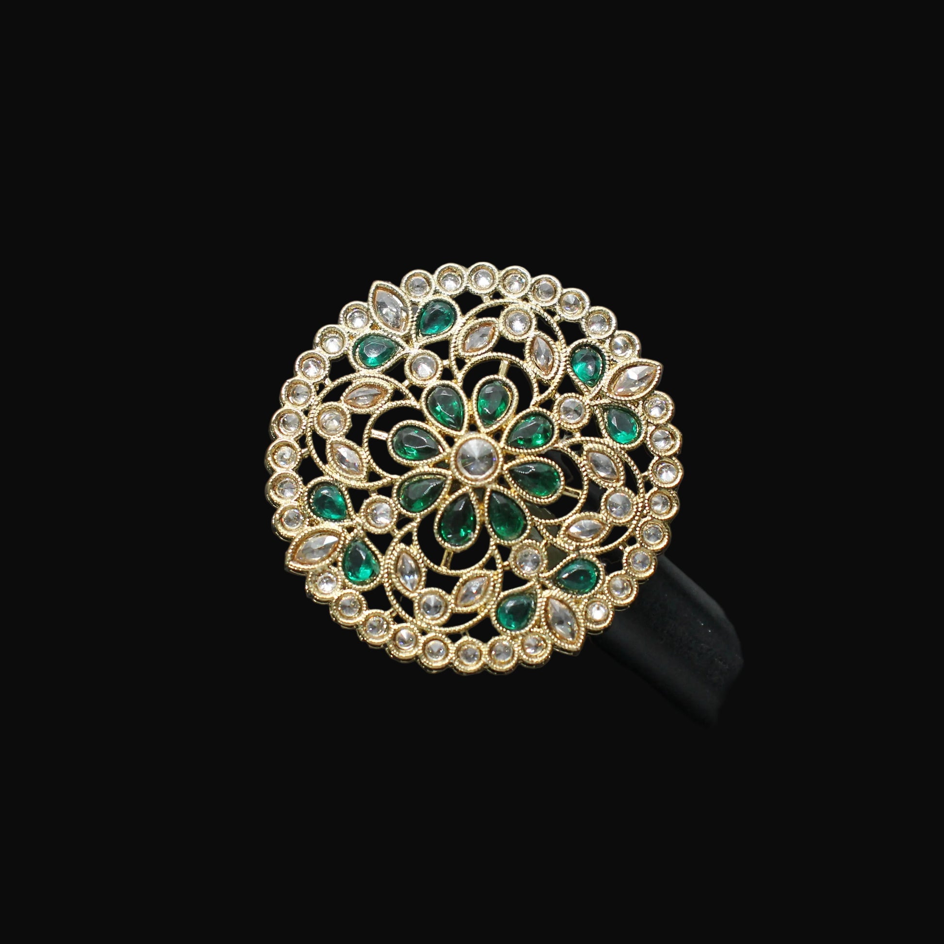 Decorative ring with green gemstones on a black mannequin hand against a dark background