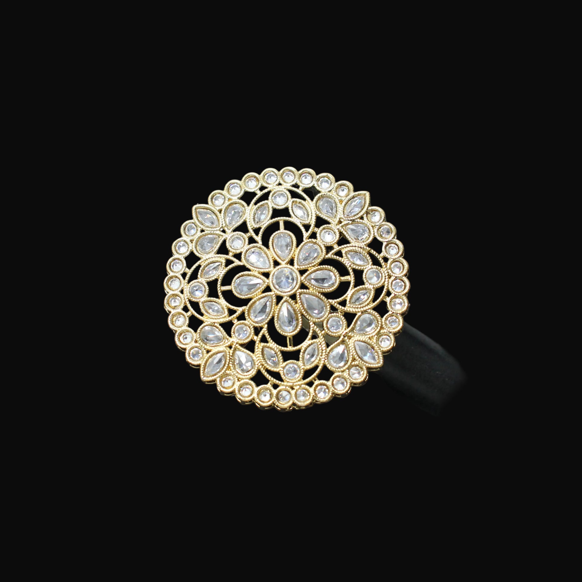 Gold and crystal brooch on a black mannequin hand against a dark background
