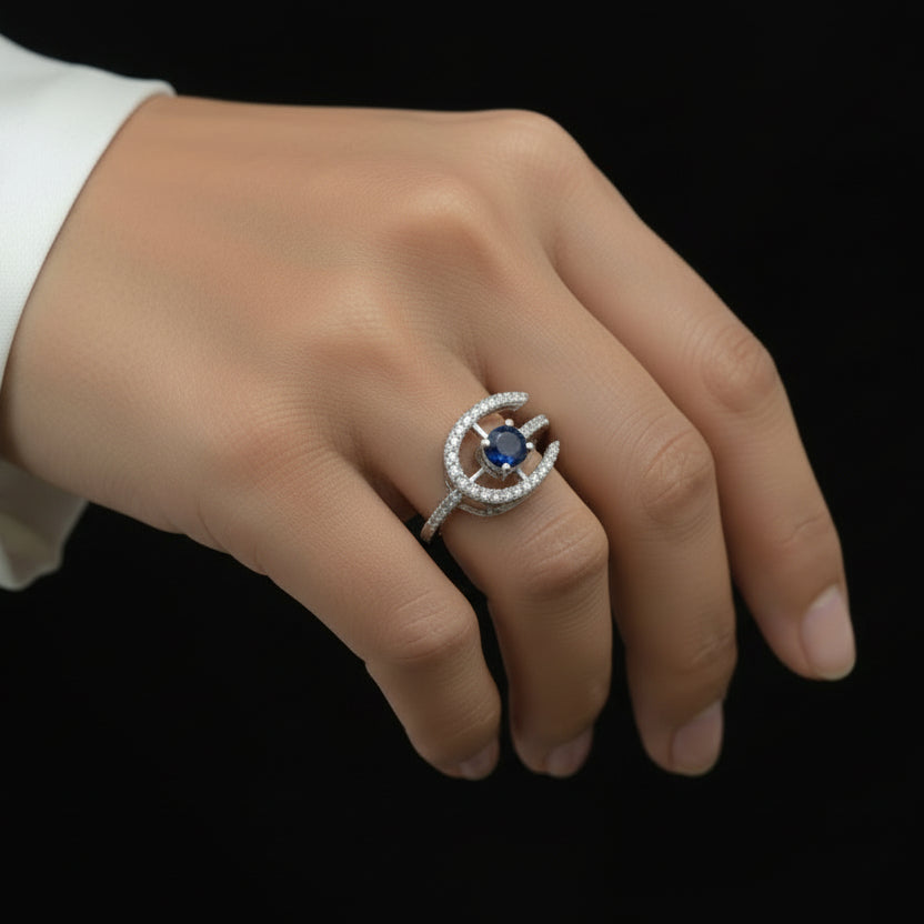Silver ring with a blue gemstone on a dark background, branded 'Saheli'.