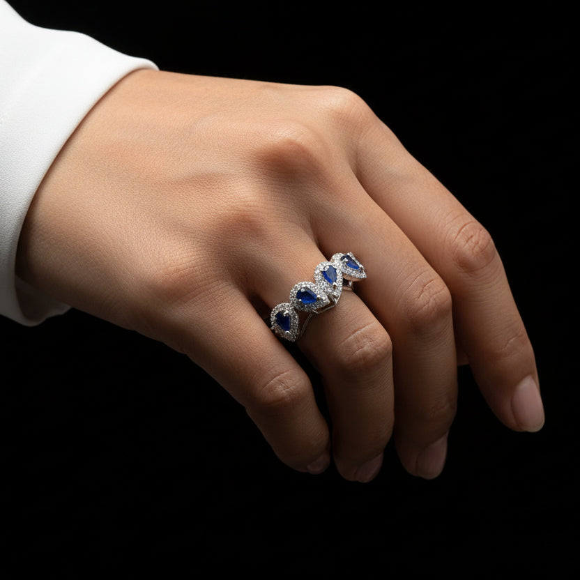 Silver ring with blue gemstones on a gray background, branded 'SAHELLI'.
