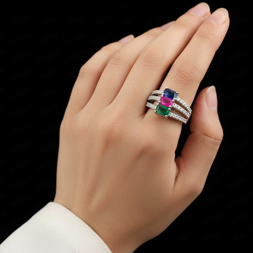 Silver ring with colored gemstones on a dark background, featuring the brand 'Saheli'.