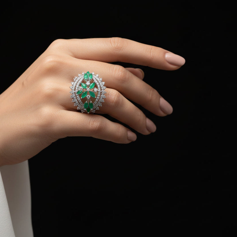 Silver ring with green gemstones on a gray background, featuring the brand 'Saheli'.