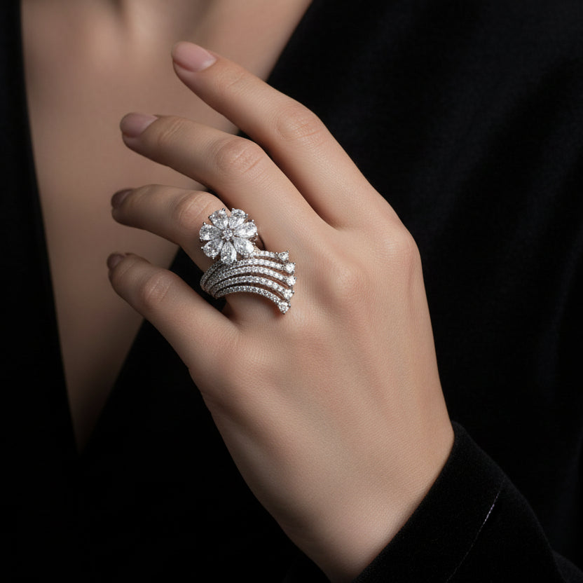 Silver ring with clear stones on a black mannequin hand, branded 'Saheli'.