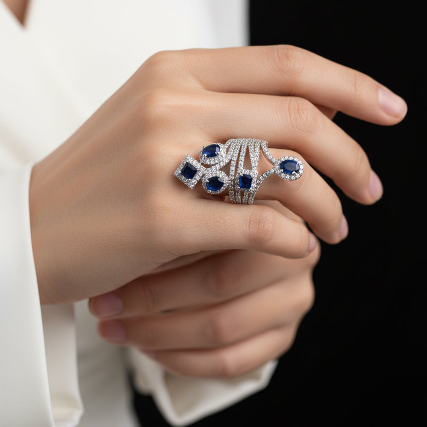 Silver brooch with blue gemstones on a gray background, featuring the brand 'SAHELI'.